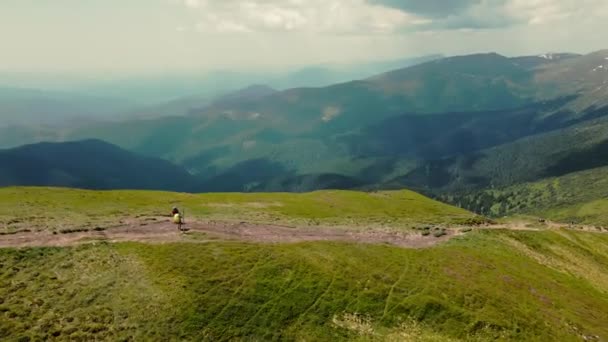 Dos excursionistas de pie en la cima de una montaña con grandes mochilas. Fondo extremadamente hermoso detrás de ellos. Vista aérea. Pintoresca belleza alrededor de las montañas circundantes — Vídeo de stock