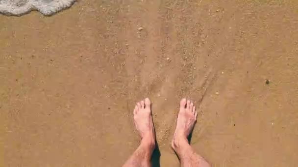 Pés masculinos junto ao mar na areia. A onda que vem para a costa lava os pés dos homens. — Vídeo de Stock