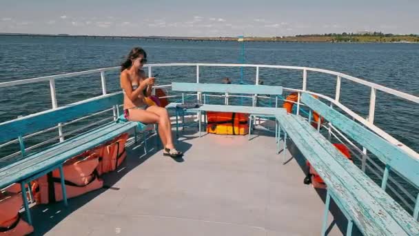 Жінка в купальнику плаває на приємному човні і тримає мобільний телефон. Самотня жінка на кораблі з телефоном в руках — стокове відео