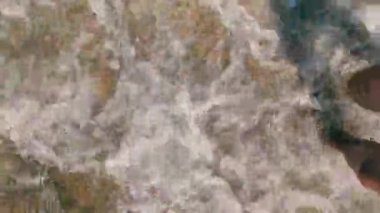 Denizin kenarında kumda duran erkek ayakları. Kıyıya gelen dalgalar adamın ayaklarını yıkar..