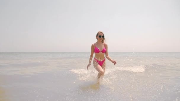 Mooi meisje loopt op het water en glimlacht. Water spatten gevormd door het lopen op water. Vakantie op zee. Eén meisje rent over het water.. — Stockvideo
