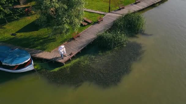 Ein Mann mit einem Mädchen und einem Regenschirm läuft den Fluss entlang. Flug über zwei Menschen, die am Fluss entlang laufen. — Stockvideo