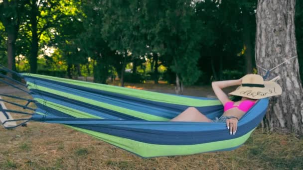 해먹으로 공원에서 쉬 세요. 수영복을 입은 한 젊은 여자 가 공원에서 모자로 머리를 덮고 잔다 — 비디오