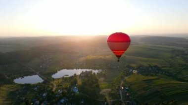 Gün batımında 2 balon gökyüzünde yüksekte uçar. Balonlar, göller ve kuş bakışı küçük bir köy ile güzel bir gün batımı. Balon güneşte uçar