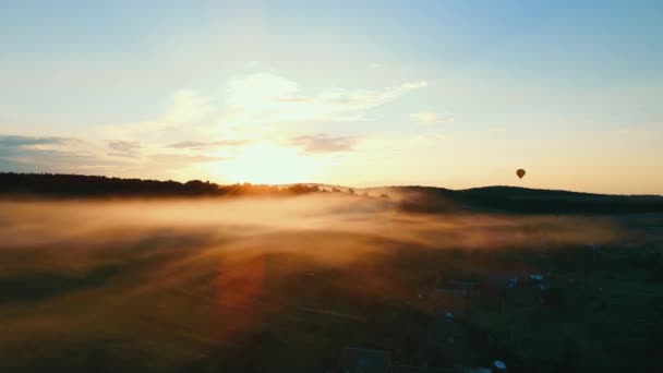 Hermoso atardecer sobre el bosque. La niebla se extiende a través de un pequeño pueblo. Un círculo aéreo volador se puede ver en el horizonte. Naranja puesta de sol y niebla ligera en movimiento — Vídeos de Stock
