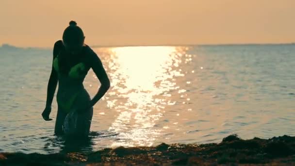 Gün doğumunda denizde yıkanan bir kadının silüeti. Kız parçaları yavaşça ovuyor ve onları deniz suyuyla yıkıyor.. — Stok video