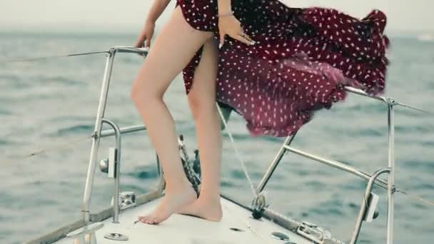 Jambes d'une jeune fille debout sur un yacht. Le vent soulève la robe bordeaux — Video