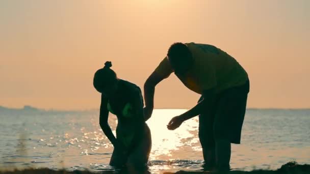 Silueta de un hombre lavando a una joven en el mar al amanecer. El hombre lava a la mujer. — Vídeos de Stock