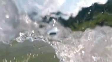 Dağ nehrinde rafting. Kamera dinamik bir şekilde sallanıyor ve su altına dalıyor, kameranın objektifine su sıçrıyor ve damlıyor..