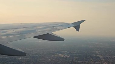 Yolcu penceresinden bakıldığında altında büyük bir şehir bulunan gümüş bir uçak kanadı görülüyor..