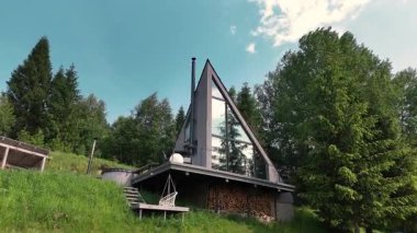 Yüksek panoramik pencereleri ve dağlardaki çimenli yamaçlara kurulmuş jakuzisi olan şık bir A çerçeveli kulübe..