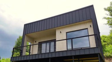 Modern kübik minimalist ev dış görünüşü koyu metal kaplama ve doğal manzaraya bakan büyük cam pencereler..