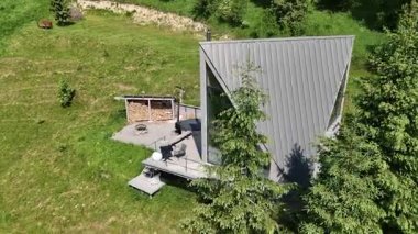 Yeşil çimenler ve çam ağaçlarıyla çevrili modern üçgen A-çerçeve kabini, ahşap kulübesi ve açık hava eğlence alanı olan minimalist tatil kiralık evi..