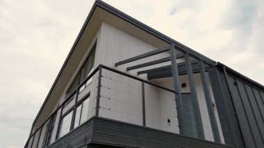 Modern A-frame kabin cephesi şık bir balkon ve minimalist siyah korkuluk, bulutlu bir gökyüzüne karşı çağdaş üçgen mimarinin alçak açılı görüntüsü.