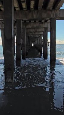 Okyanus rıhtımının altında, sakin su yansımalarıyla, yukarıdaki yapıyı yansıtan okyanus dalgaları olan bir rıhtım manzarası.