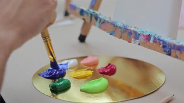 Sanatçı, mavi boyayı stüdyodaki altın palette fırçayla karıştırıyor, yaratıcı ressam renkli akrilik boyaları tuvale çizmek için hazırlıyor..