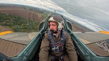 Askeri pilot savaş uçağını yeşil tarlaların ve köyün üzerinden uçuruyor, alçak irtifa uçuş görevinde kokpitten manzarası var..
