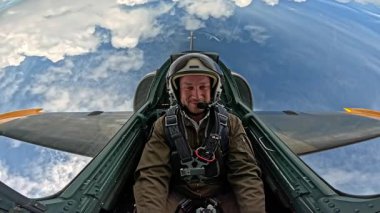 Miğferli ve uçuş kostümlü profesyonel erkek pilot jet kokpitinde oturuyor, askeri pilot bulutların üzerinde mavi gökyüzünde uçuyor..