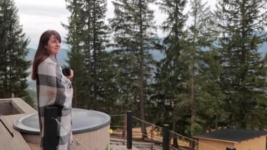 Dağ balkonunda elinde kahve fincanı olan mutlu kadın, sabah manzarasını seviyor..