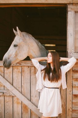 Güneşli bir günde çiftlikte poz veren şapkalı ve elbiseli genç bir kız.