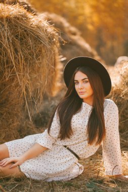Güneşli bir günde çiftlikte poz veren şapkalı ve elbiseli genç bir kız.