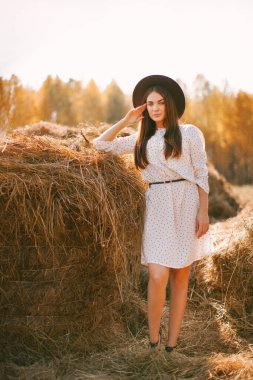 Güneşli bir günde çiftlikte poz veren şapkalı ve elbiseli genç bir kız.