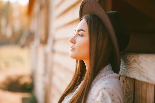 Güneşli bir günde çiftlikte poz veren şapkalı ve elbiseli genç bir kız.