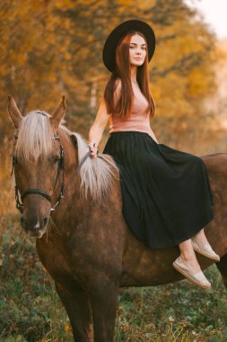 Doğada ata binen şapkalı bir kız.