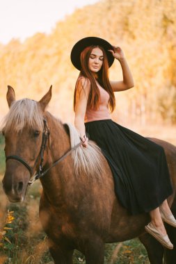 Doğada ata binen şapkalı bir kız.