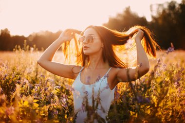 Kolsuz tişörtlü genç bir esmer ve çimlerin üzerinde gün batımına karşı poz veren şortlu.