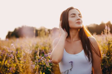 Kolsuz tişörtlü genç bir esmer ve çimlerin üzerinde gün batımına karşı poz veren şortlu.
