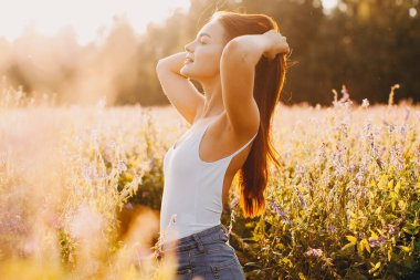 Kolsuz tişörtlü genç bir esmer ve çimlerin üzerinde gün batımına karşı poz veren şortlu.