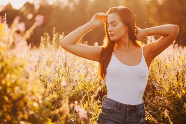 Kolsuz tişörtlü genç bir esmer ve çimlerin üzerinde gün batımına karşı poz veren şortlu.