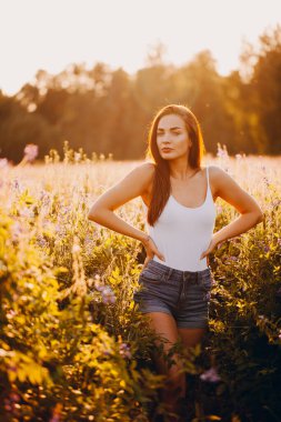 Kolsuz tişörtlü genç bir esmer ve çimlerin üzerinde gün batımına karşı poz veren şortlu.