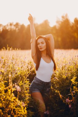 Kolsuz tişörtlü genç bir esmer ve çimlerin üzerinde gün batımına karşı poz veren şortlu.