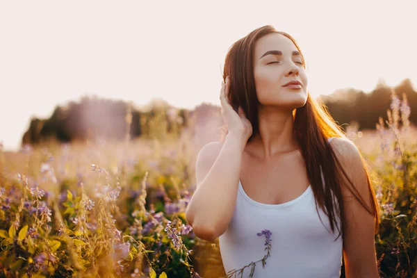 Kolsuz tişörtlü genç bir esmer ve çimlerin üzerinde gün batımına karşı poz veren şortlu.