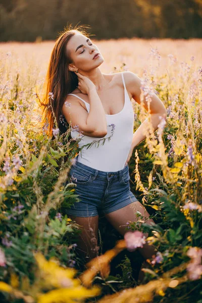 Kolsuz tişörtlü genç bir esmer ve çimlerin üzerinde gün batımına karşı poz veren şortlu.