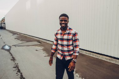 Şehirde yürüyen ekose gömlekli mutlu bir zenci portresi.