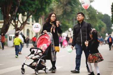 Hanoi, Vietnam 13 Ocak 2018: Bebek arabasında kızı ve çocuğu olan genç bir aile, sokakta elinde topla yürüyor..