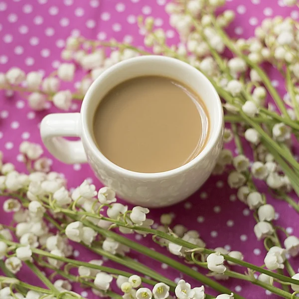 Filiżankę kawy z mlekiem, mayflowers na polka-dotted różowy tablecl — Zdjęcie stockowe