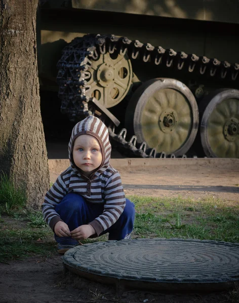 Niño pequeño agachado al lado del tanque — Foto de Stock