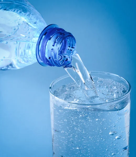 Wasser aus Flasche in Glas auf blauem Hintergrund gießen — Stockfoto