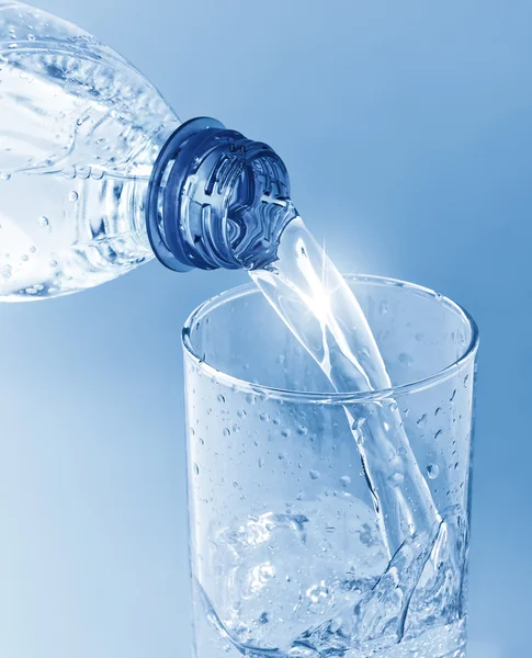 Wasser aus Flasche in Glas auf blauem Hintergrund gießen — Stockfoto