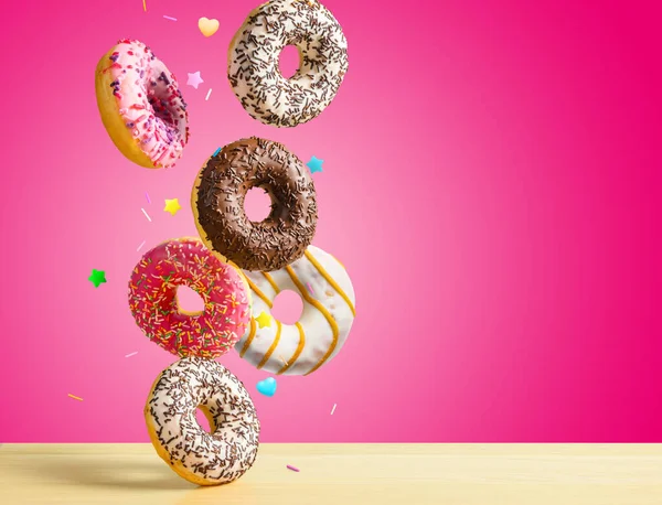 Fliegende Donuts. Mischung aus bunten süßen Krapfen mit Streusel auf rosa Hintergrund fällt auf den Tisch. — Stockfoto