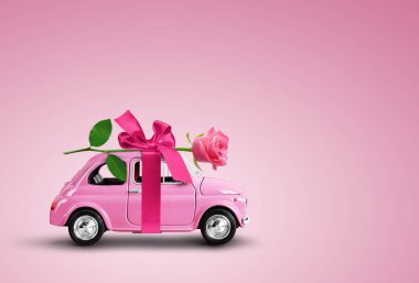 Pembe oyuncak araba pembe arka planda pembe gül çiçeği getiriyor. Çiçek teslimatı, kadınlar günü, sevgililer günü.