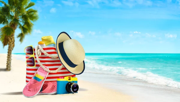 Καλοκαιρινή τσάντα θαλάσσης και αξεσουάρ - ψάθινο καπέλο, σαγιονάρες και γυαλιά ηλίου σε αμμώδη παραλία και γαλάζια θάλασσα στο φόντο — Φωτογραφία Αρχείου