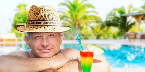 A man is enjoying his vacation relaxing with refreshing drink on the pool on resort hotel background.