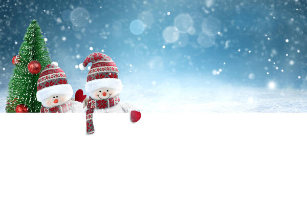 Two Cute Snowmen with blank banner on snowy landscape background