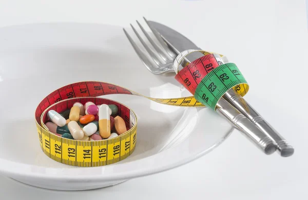 Conceito de dieta. fita métrica embrulhada Twith comprimidos em uma placa . — Fotografia de Stock