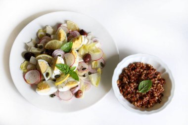 Beyaz zemin üzerinde hindiba, haşlanmış yumurta, turp, soğan, zeytin, limon, ayçiçeği tohumu ve farro (emmer) salatası bulunan taze salata. Sağlıklı yemek..